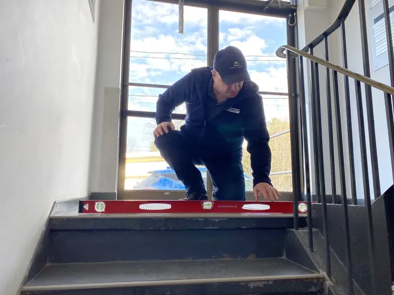 Christophe Muller vérifiant le niveau des escaliers lors d'une inspection de bâtiment