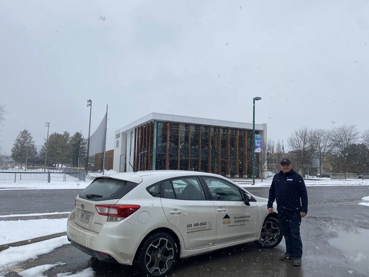 Inspecteur en bâtiment posant avec son véhicule de service sur le stationnement de l'hôtel de ville, devant la bibliothèque Paul-Mercier sous la neige à Blainville.