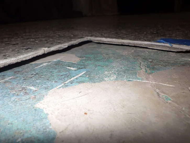 Inspection d'un problème d'humidité montrant un décollement de revêtement d'époxy sur dalle de béton.
