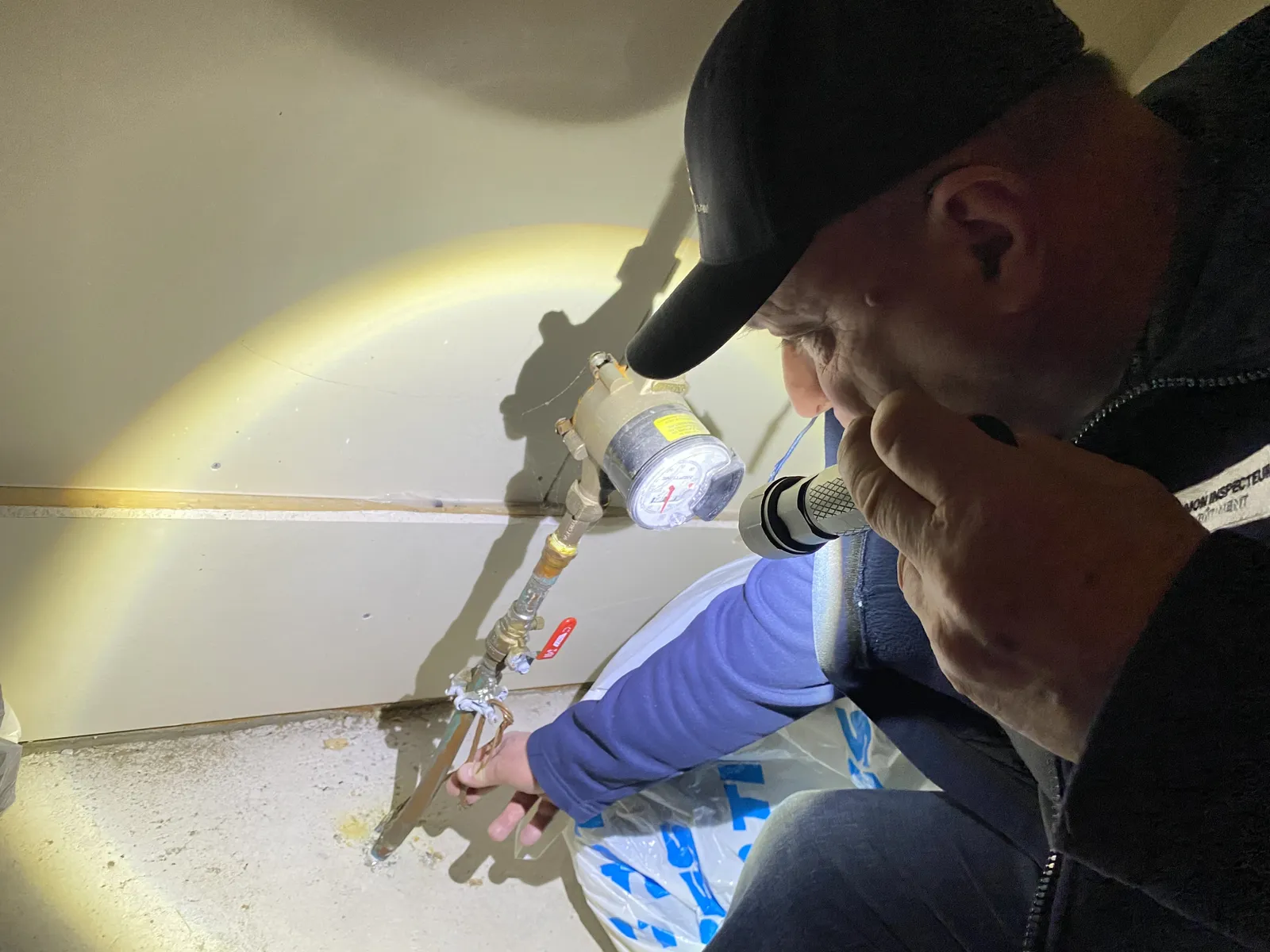Christophe Muller examinant la plomberie et les raccords d'un chauffe-eau lors d'une inspection à Auteuil, Laval.