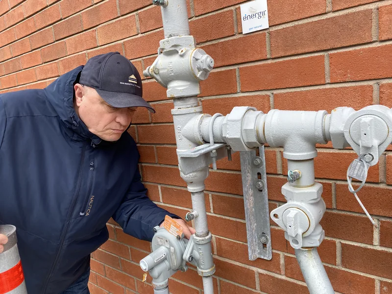 Inspecteur en bâtiment certifié effectuant une observation d'un régulateur de pression et de l'entrée de gaz à Sainte-Anne-des-Plaines.